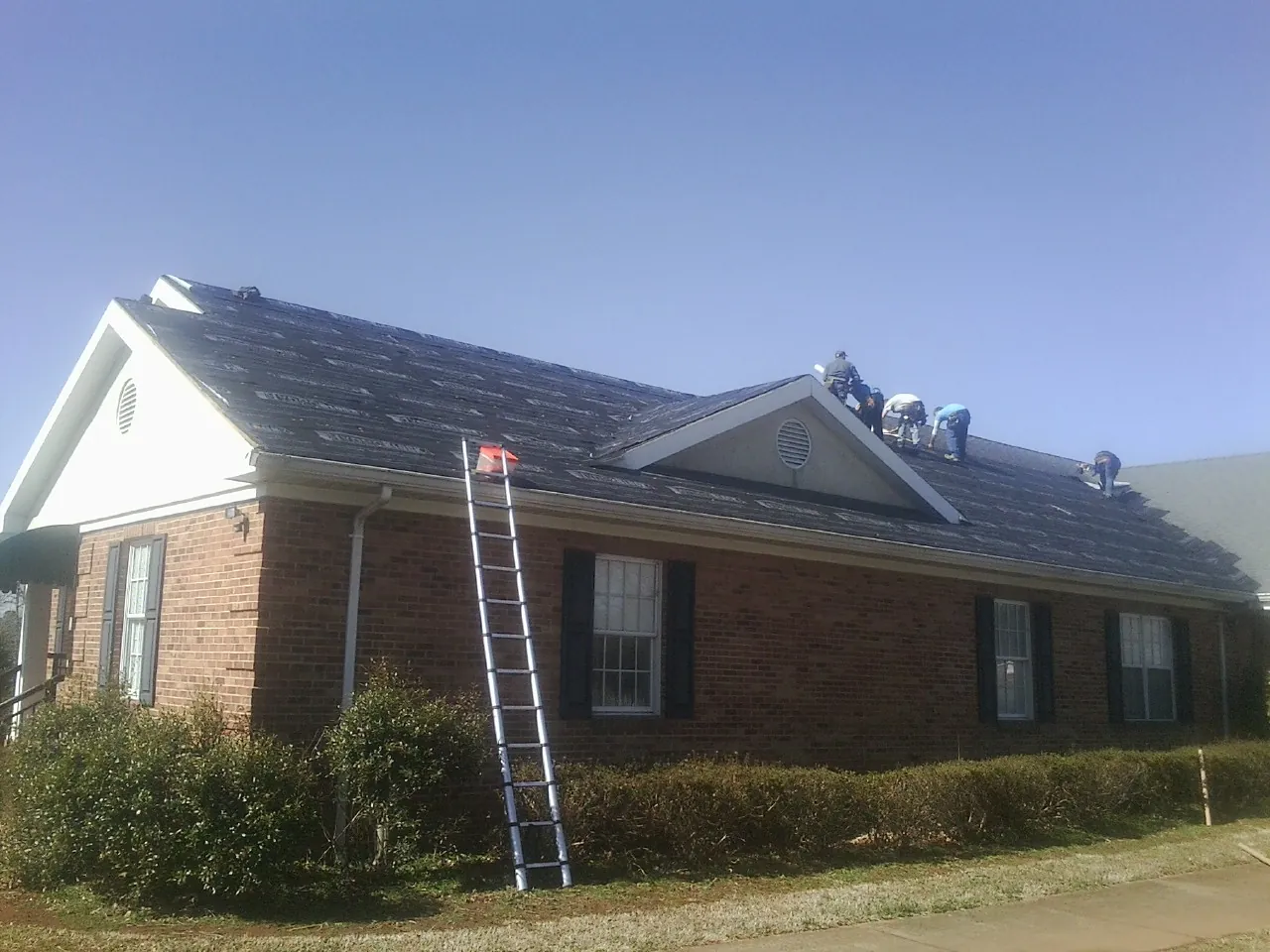 Crew tearing shingles off a brick ranch roof with a ladder set — Metal Roof Repair work by our crew in Cambridge
